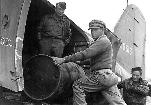 Three men loading barrel into transport plane