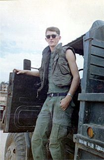 Young soldier in sunglasses leaning on military truck